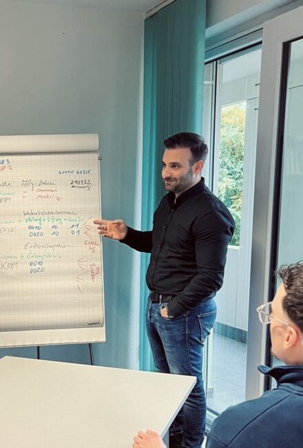 AGENA-Mitarbeiter präsentiert Kollegen seine Ausarbeitungen an einem Flipchart.