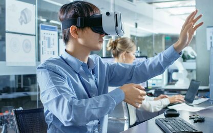 Person mit VR-Brille in modernem Büro, im Hintergrund Computerarbeit






