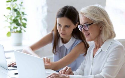 Zwei Frauen arbeiten gemeinsam an einem Laptop in einem hellen Büro