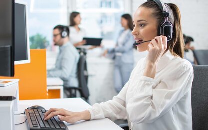 Freundliche weibliche Kundendienstmitarbeiterin trägt ein Headset und arbeitet am Schreibtisch